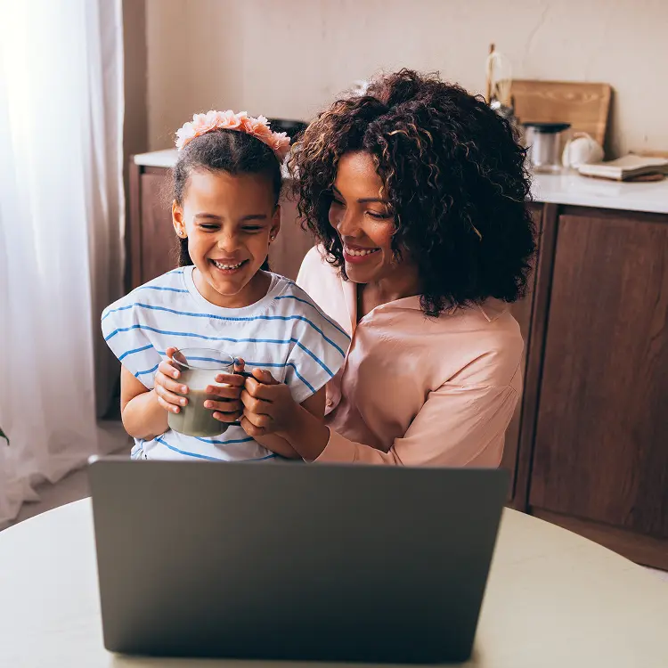 Woman holding her daughter in lap while looking at laptop