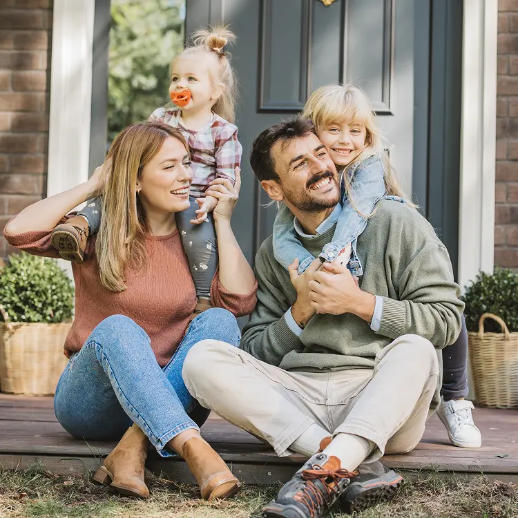 Mother and Father sitting on front porch with their daughters climbing on each of them